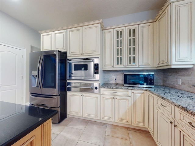 kitchen with decorative backsplash, light tile patterned floors, light stone counters, stainless steel appliances, and cream cabinets