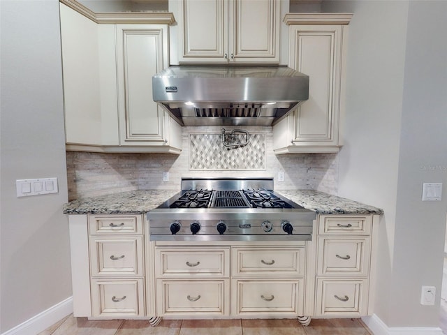 kitchen with range hood, stainless steel gas stovetop, decorative backsplash, light stone countertops, and cream cabinetry