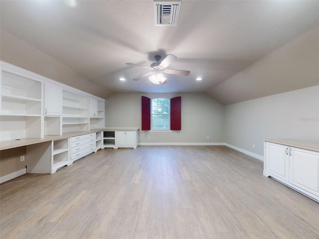 additional living space with light hardwood / wood-style flooring, ceiling fan, built in desk, a textured ceiling, and vaulted ceiling