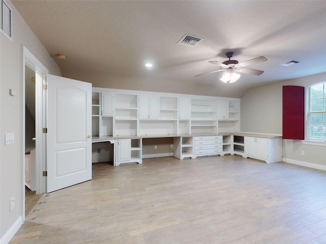 unfurnished office featuring lofted ceiling, built in desk, ceiling fan, and light hardwood / wood-style flooring