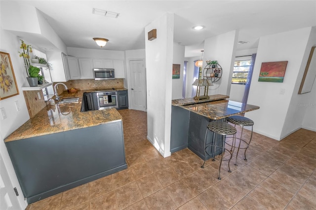 kitchen featuring appliances with stainless steel finishes, white cabinets, kitchen peninsula, and sink