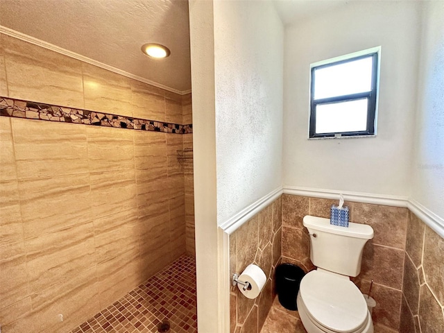 bathroom featuring toilet, a tile shower, tile patterned flooring, tile walls, and a textured ceiling