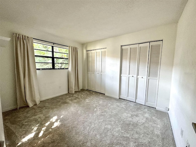 unfurnished bedroom featuring a textured ceiling, multiple closets, and light carpet