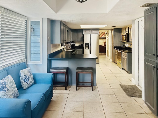 kitchen featuring appliances with stainless steel finishes, sink, gray cabinetry, light tile patterned floors, and kitchen peninsula