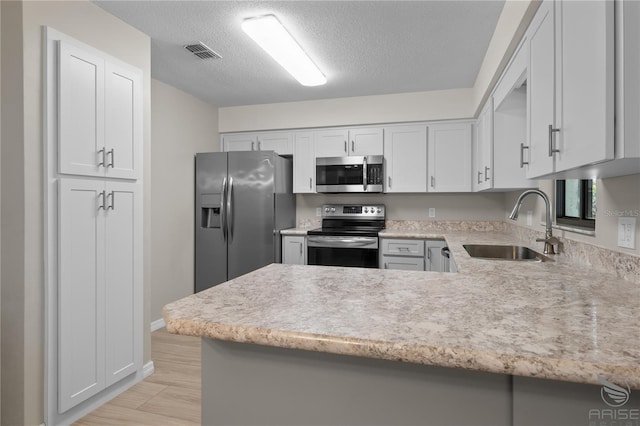 kitchen featuring appliances with stainless steel finishes, sink, a textured ceiling, and kitchen peninsula