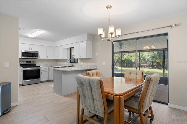 dining area featuring ceiling fan with notable chandelier, light hardwood / wood-style floors, sink, and a textured ceiling