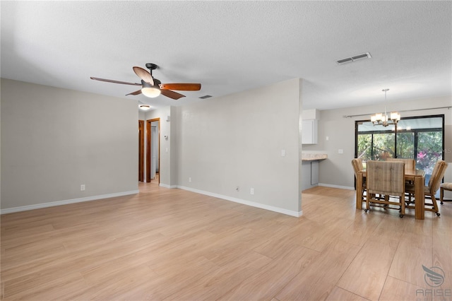 unfurnished living room featuring ceiling fan with notable chandelier, light hardwood / wood-style floors, and a textured ceiling