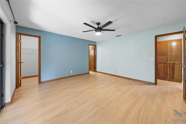 unfurnished bedroom with ceiling fan, a closet, light hardwood / wood-style flooring, and a walk in closet