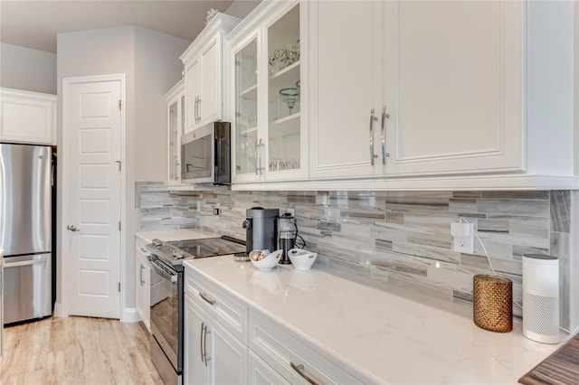 kitchen with stainless steel appliances, white cabinetry, light stone counters, and backsplash