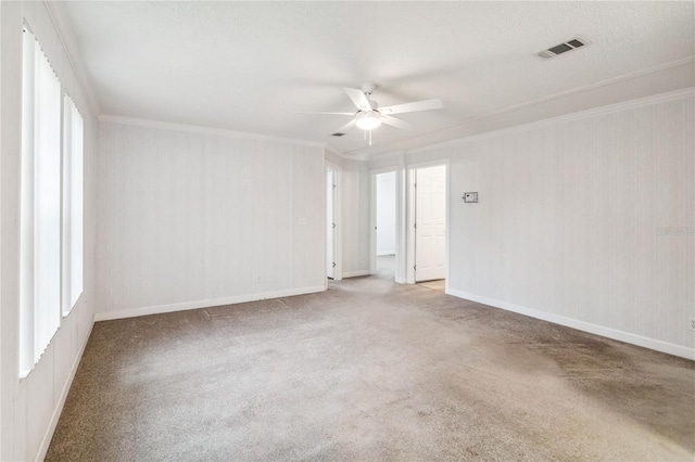 carpeted spare room with baseboards, ceiling fan, visible vents, and crown molding