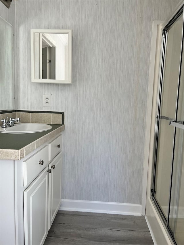 bathroom featuring wallpapered walls, wood finished floors, baseboards, and vanity