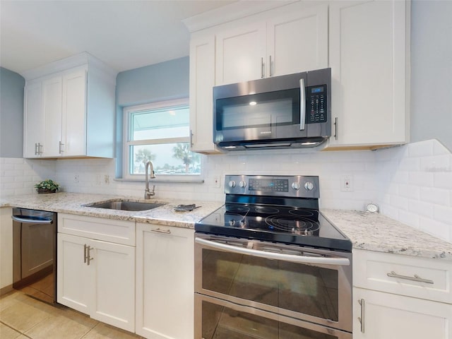 kitchen with white cabinetry, sink, light tile patterned floors, stainless steel appliances, and light stone countertops