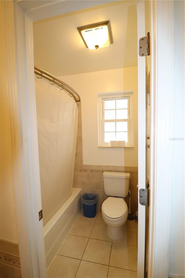 bathroom with tile walls, tile patterned floors, shower / bath combo with shower curtain, and toilet