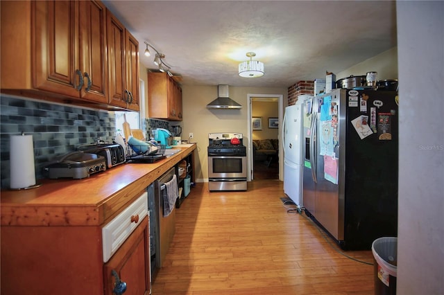 kitchen featuring wall chimney range hood, butcher block countertops, light hardwood / wood-style flooring, stainless steel appliances, and tasteful backsplash