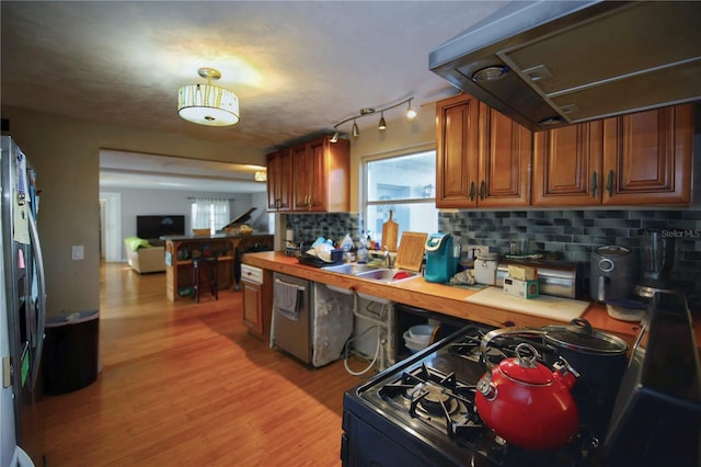 kitchen with extractor fan, appliances with stainless steel finishes, tasteful backsplash, sink, and light wood-type flooring