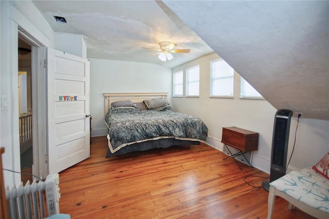 bedroom with radiator heating unit, hardwood / wood-style flooring, vaulted ceiling, and ceiling fan