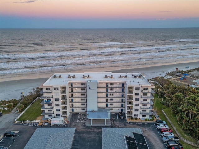 aerial view at dusk featuring a view of the beach and a water view