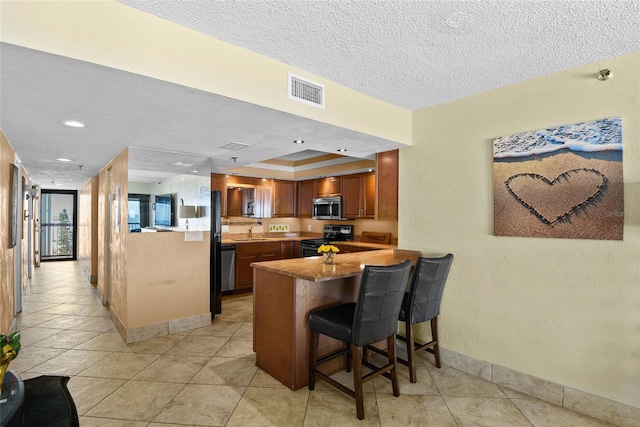 kitchen featuring light tile patterned floors, appliances with stainless steel finishes, a kitchen breakfast bar, a tray ceiling, and kitchen peninsula