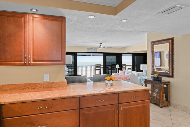 kitchen with light tile patterned floors, ceiling fan, light stone countertops, a textured ceiling, and kitchen peninsula