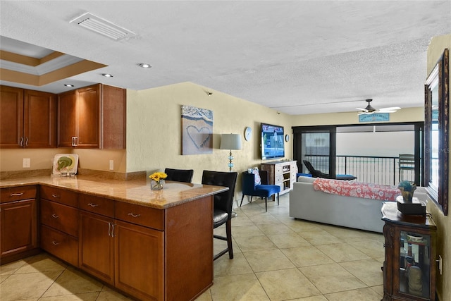 kitchen with light tile patterned floors, a breakfast bar, light stone countertops, a textured ceiling, and kitchen peninsula