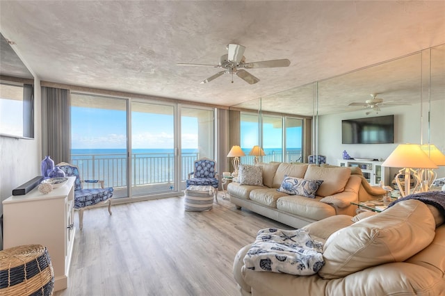 living room featuring expansive windows, a water view, ceiling fan, and light hardwood / wood-style floors