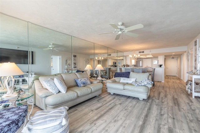 living room with ceiling fan with notable chandelier and light hardwood / wood-style flooring