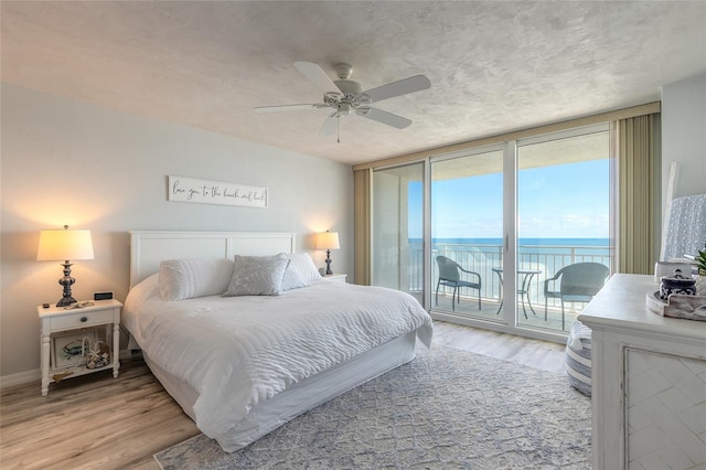 bedroom featuring a water view, ceiling fan, light hardwood / wood-style flooring, and access to outside