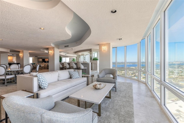 tiled living room with a water view, a textured ceiling, and a wall of windows