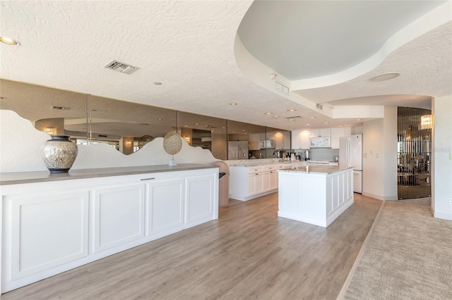 kitchen with decorative light fixtures, white cabinetry, a kitchen island with sink, light hardwood / wood-style floors, and white appliances