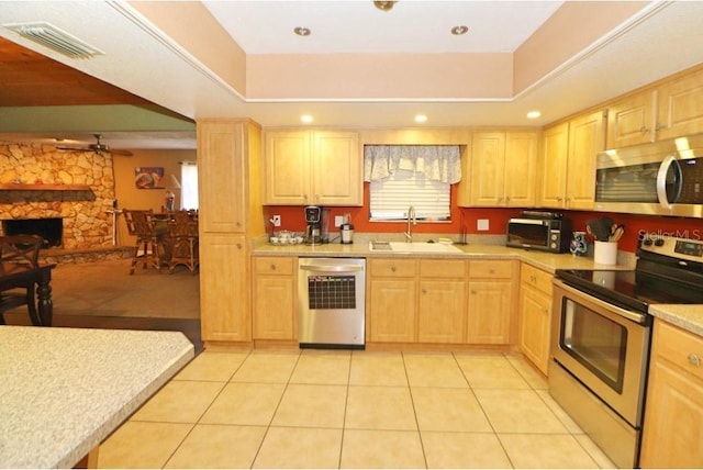 kitchen featuring a stone fireplace, light brown cabinetry, sink, light tile patterned floors, and stainless steel appliances