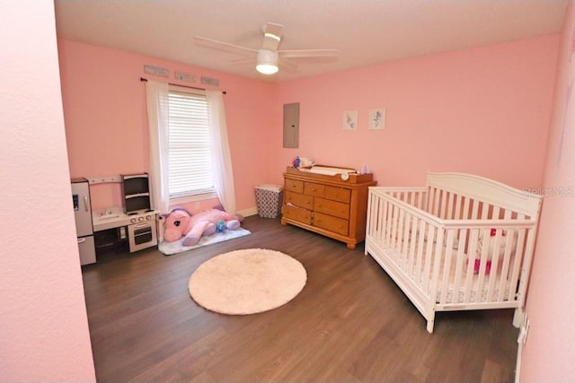 bedroom featuring a crib, electric panel, dark hardwood / wood-style floors, and ceiling fan