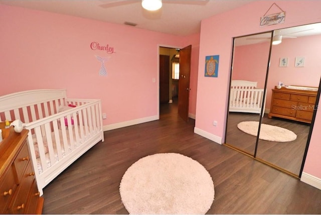 bedroom featuring a nursery area, dark wood-type flooring, ceiling fan, and a closet