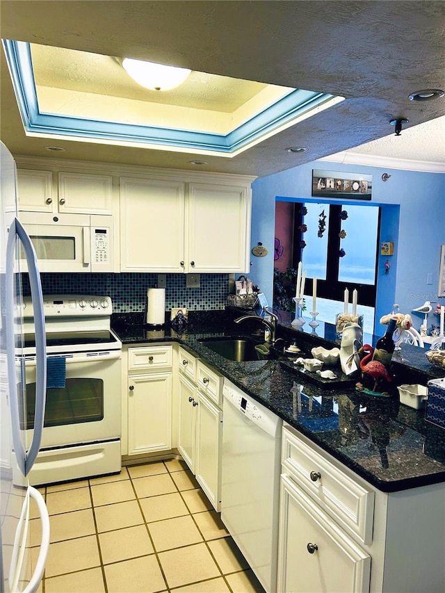 kitchen featuring sink, white appliances, dark stone countertops, a tray ceiling, and ornamental molding