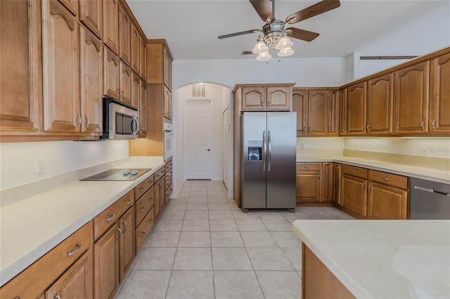 kitchen with appliances with stainless steel finishes, arched walkways, brown cabinets, and light countertops