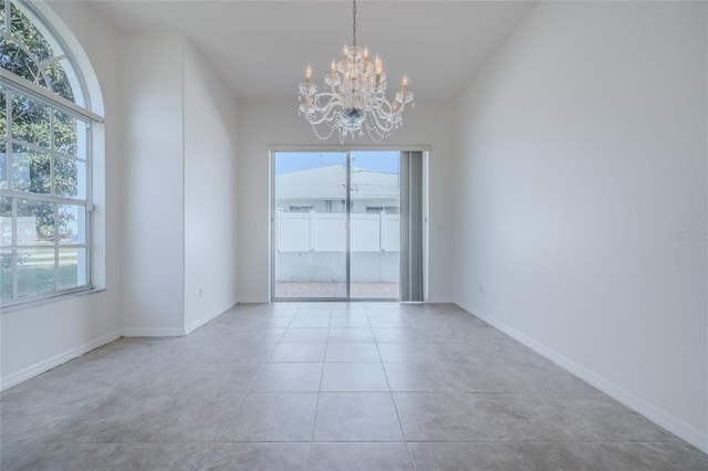 empty room featuring a healthy amount of sunlight, an inviting chandelier, tile patterned flooring, and baseboards