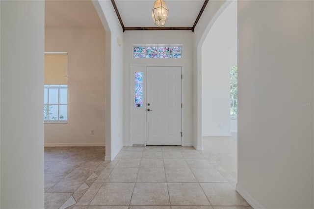 foyer featuring light tile patterned floors, baseboards, arched walkways, and crown molding