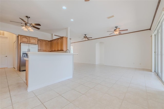 kitchen featuring arched walkways, crown molding, light tile patterned floors, light countertops, and stainless steel fridge