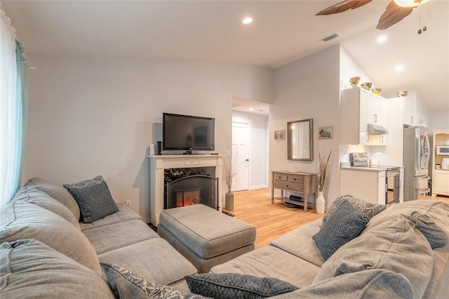 living room with ceiling fan, lofted ceiling, a fireplace, and light hardwood / wood-style flooring