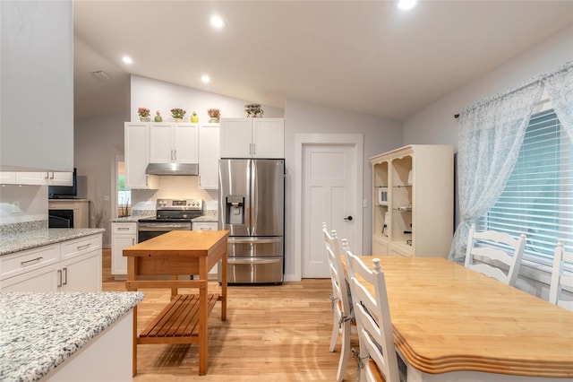 kitchen with appliances with stainless steel finishes, lofted ceiling, white cabinets, light stone countertops, and light hardwood / wood-style flooring