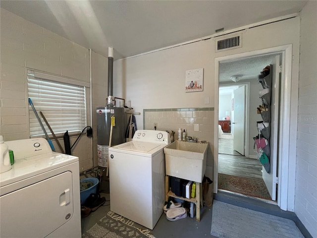 clothes washing area with tile walls, gas water heater, and washing machine and clothes dryer