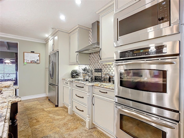 kitchen with wall chimney exhaust hood, light stone counters, tasteful backsplash, ornamental molding, and appliances with stainless steel finishes