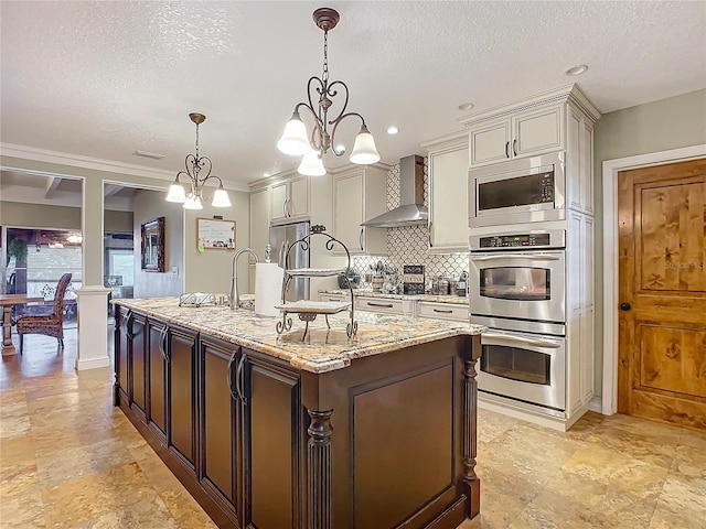 kitchen featuring light stone counters, tasteful backsplash, hanging light fixtures, stainless steel appliances, and wall chimney range hood