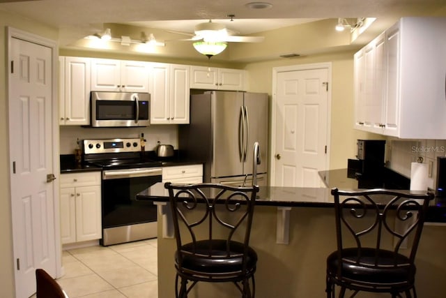 kitchen with a breakfast bar area, light tile patterned floors, kitchen peninsula, stainless steel appliances, and white cabinets