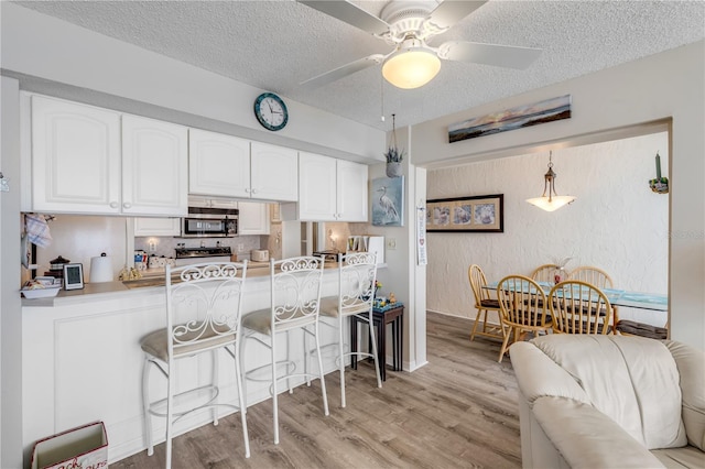 kitchen featuring decorative light fixtures, white cabinetry, a kitchen bar, a textured ceiling, and light hardwood / wood-style flooring