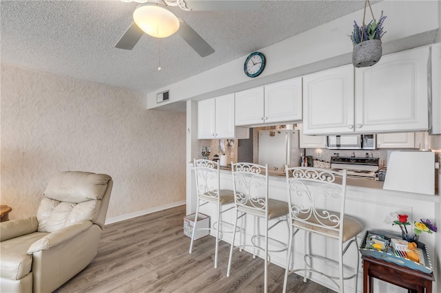 kitchen with light hardwood / wood-style flooring, a breakfast bar area, appliances with stainless steel finishes, a textured ceiling, and white cabinets