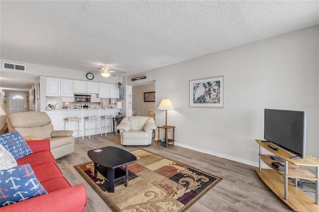 living room featuring ceiling fan, light hardwood / wood-style floors, and a textured ceiling