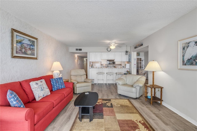 living room featuring ceiling fan, a textured ceiling, and light hardwood / wood-style flooring