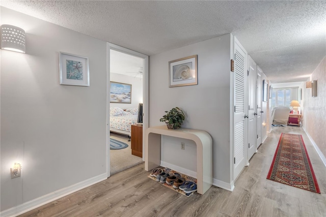 hallway with a textured ceiling and light hardwood / wood-style flooring