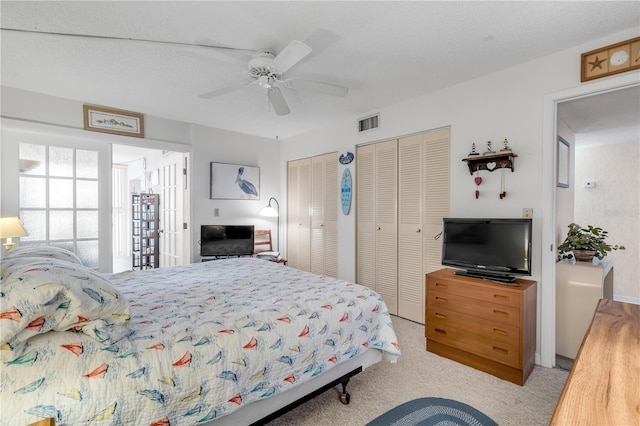 bedroom featuring multiple closets, ceiling fan, light colored carpet, and a textured ceiling