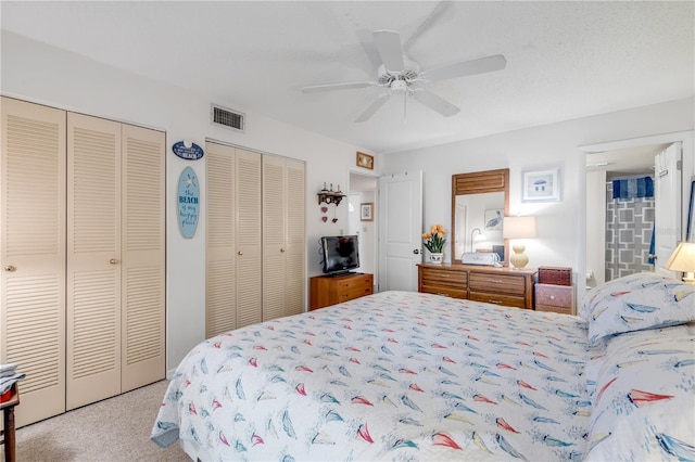 bedroom with ceiling fan, a textured ceiling, light carpet, and two closets